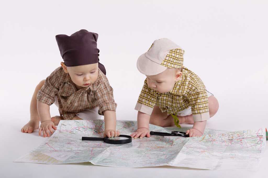 Two babies playing on top of a large map, with two magnifying glasses on the map as if they were toys